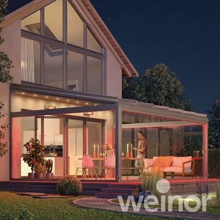 Modernes Einfamilienhaus mit beleuchtetem Wintergarten und gemütlicher Terrasse bei Nacht.