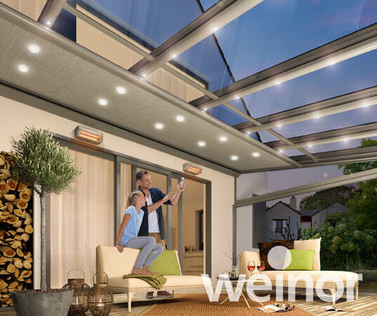 Modernes Terrassendach aus Glas mit LED-Beleuchtung und gemütlicher Sitzgruppe im Garten.